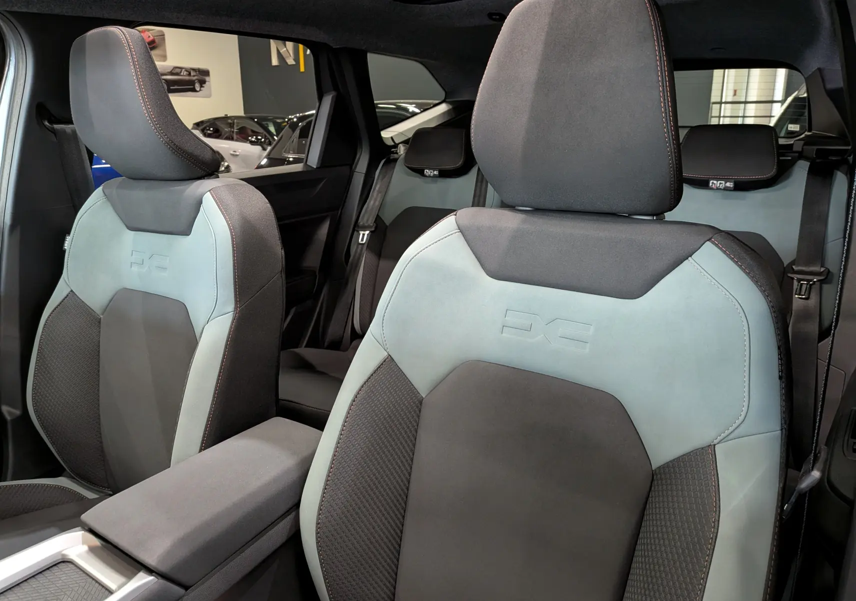 Vue intérieure rapprochée des sièges avant gris et bleu clair du Dacia Bigster Hybrid-G 150 4x4, avec surpiqûres orange.