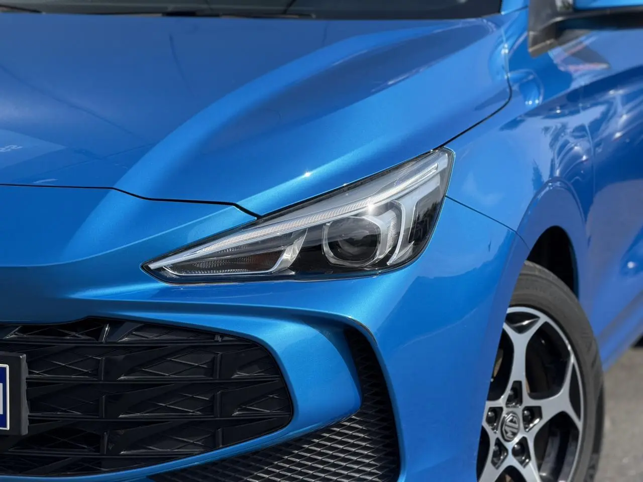 Gros plan sur l’avant droit du MG3 1.5 Hybrid+ 195 Comfort bleu Como, mettant en valeur le phare LED et la calandre noire.