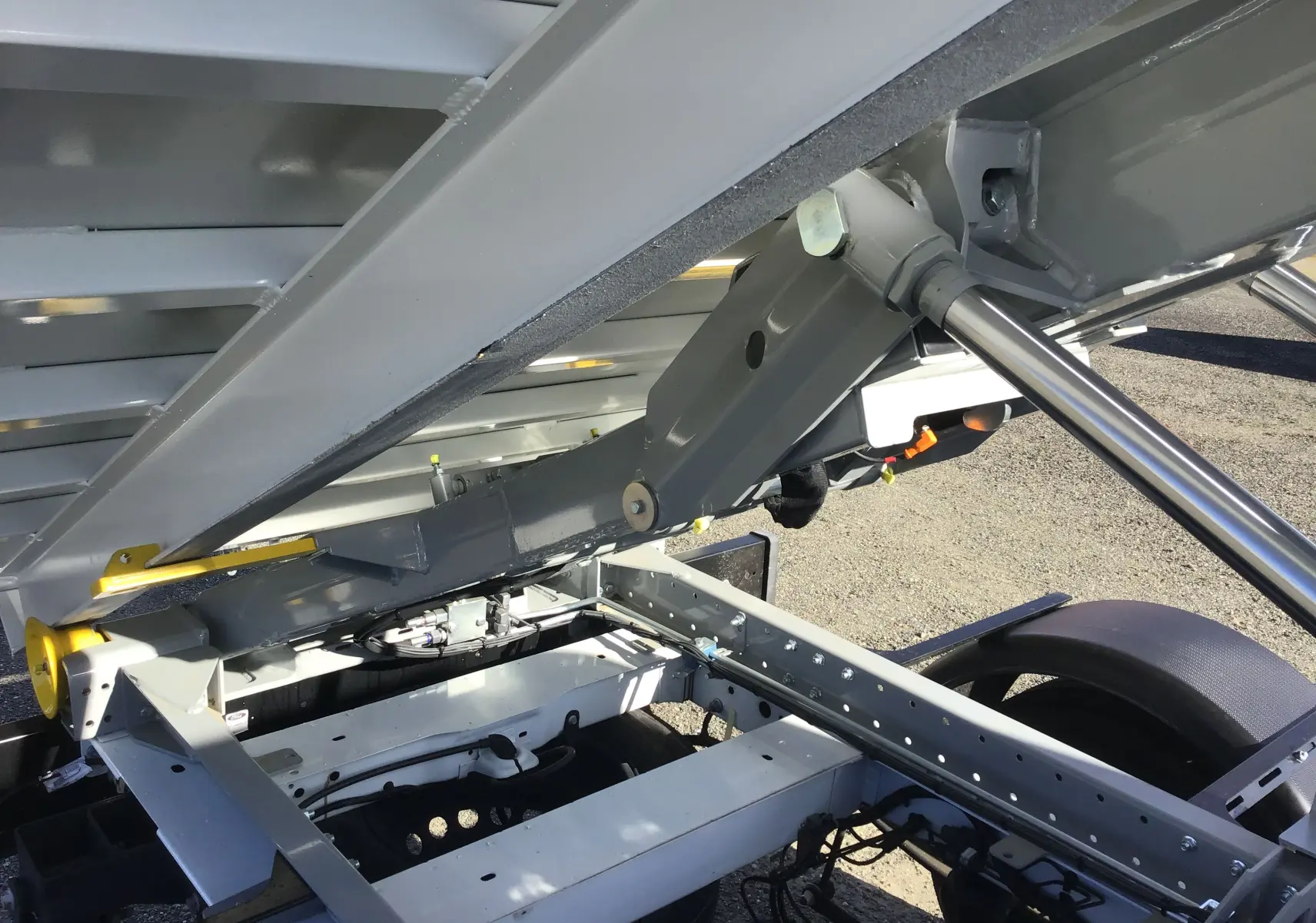 Gros plan sur le mécanisme gris du bras polybenne relevé du Ford Transit Châssis Cabine blanc, côté arrière droit.