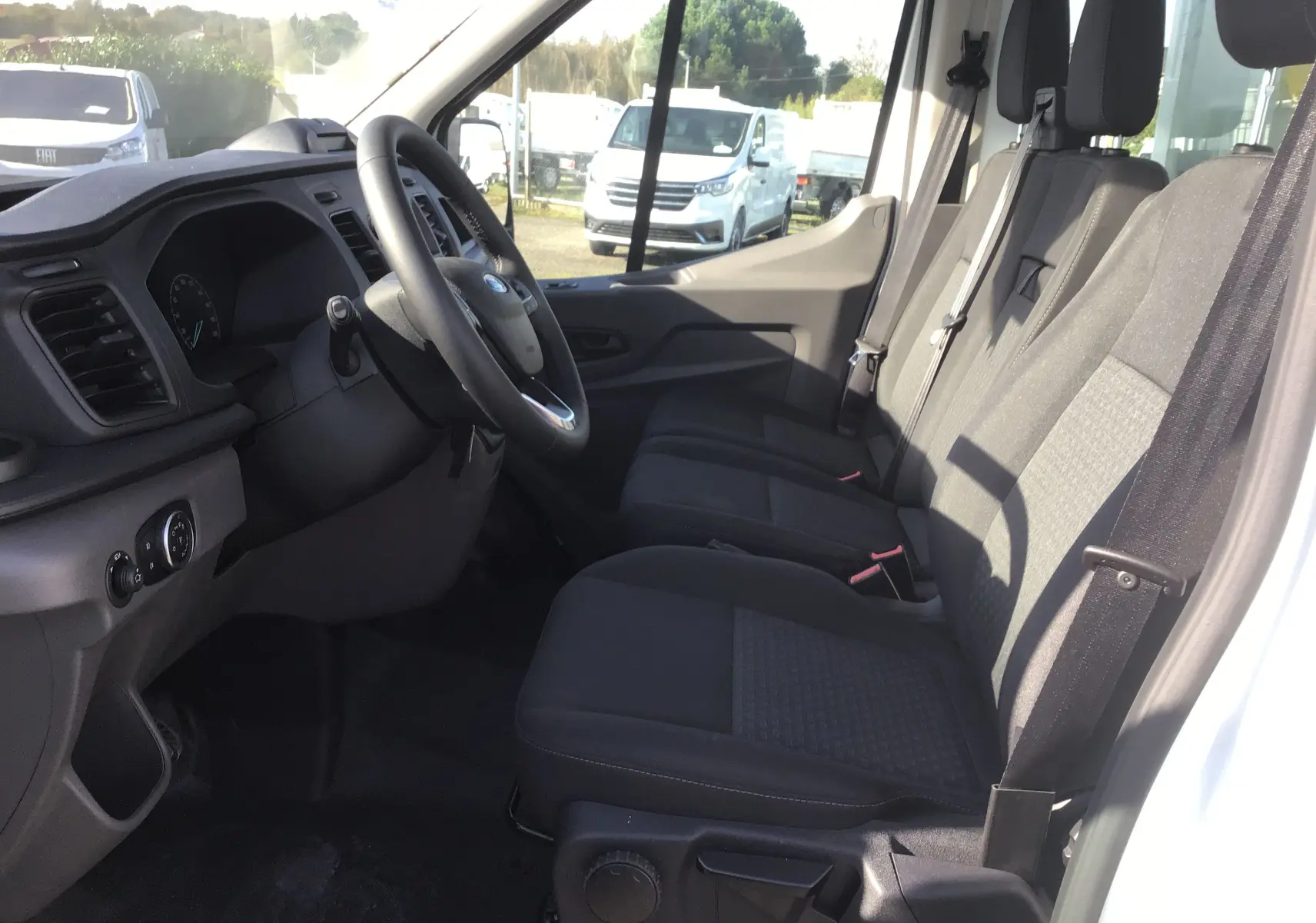 Intérieur côté conducteur du Ford Transit Châssis Cabine blanc, montrant les sièges noirs et le tableau de bord moderne.