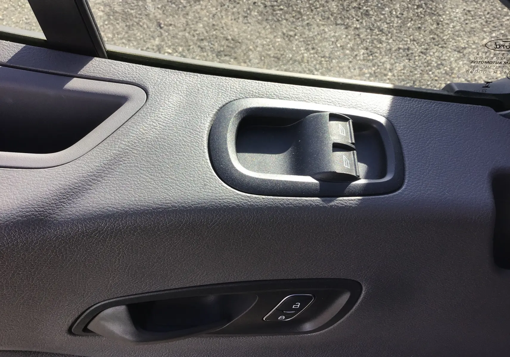 Gros plan sur la porte côté gauche du Ford Transit blanc, montrant les commandes des vitres et la poignée intérieure.