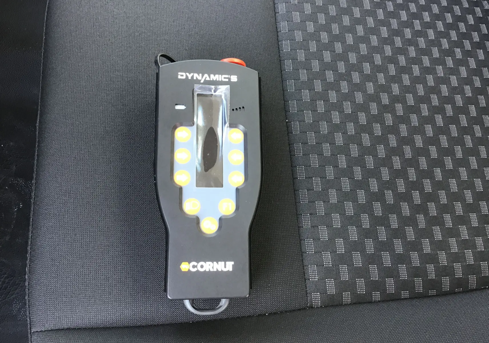 Télécommande noire Dynamics Cornut posée sur un siège tissu gris et noir, intérieur d'un Ford Transit Châssis Cabine blanc.