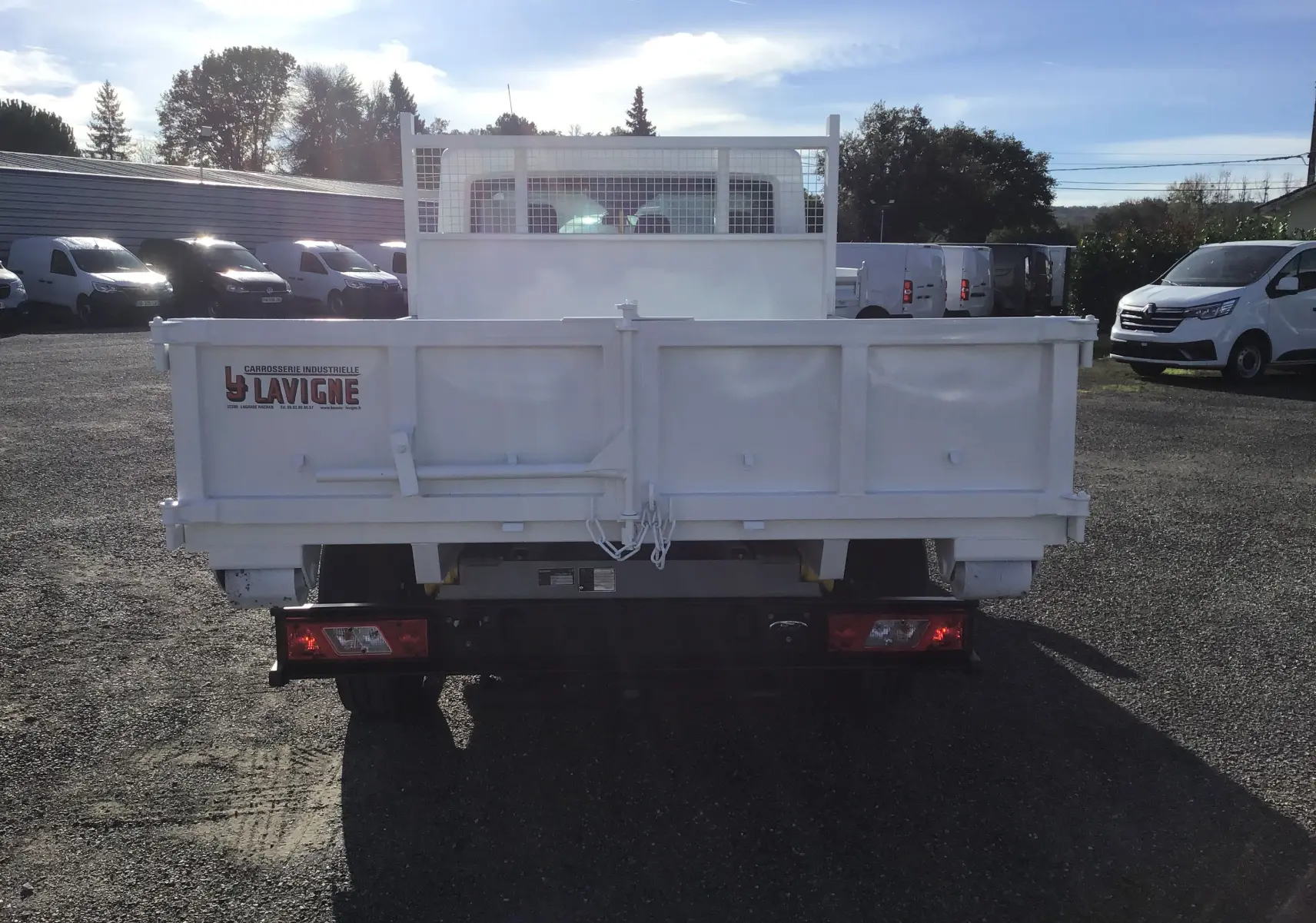 Vue arrière d'un Ford Transit Châssis Cabine blanc avec benne 3m20 et grillage protecteur de cabine.