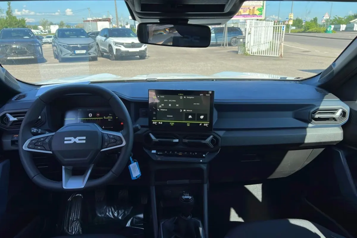 Vue intérieure du tableau de bord du Dacia Bigster blanc glacier 2025, avec écran tactile central et volant multifonction.