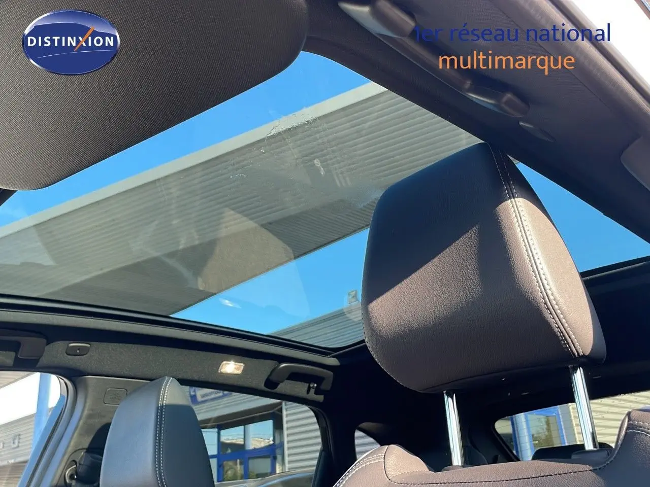 Vue intérieure du Nissan Qashqai 2025 blanc nacré avec toit panoramique et appuie-tête en cuir noir visible.