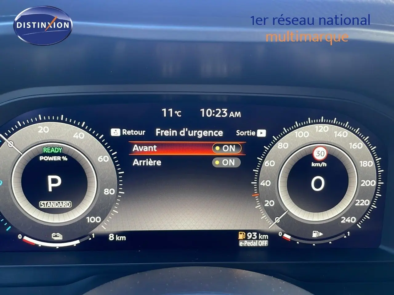 Tableau de bord numérique du Nissan Qashqai blanc nacré, affichant le frein d'urgence activé à 10h23.