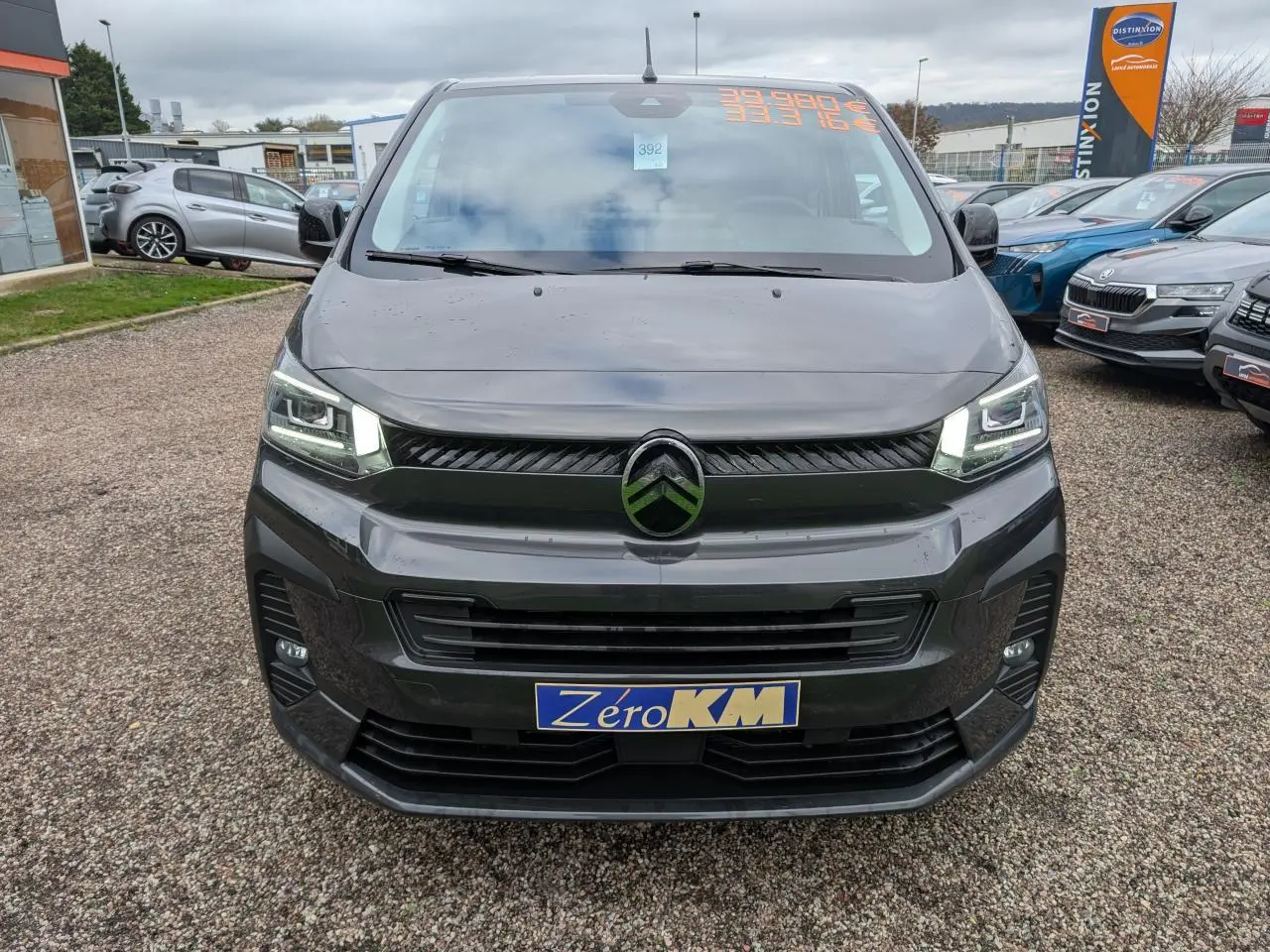 Vue frontale d'un Citroën Jumpy gris avec phares LED allumés et plaque Zéro KM sur un parking.