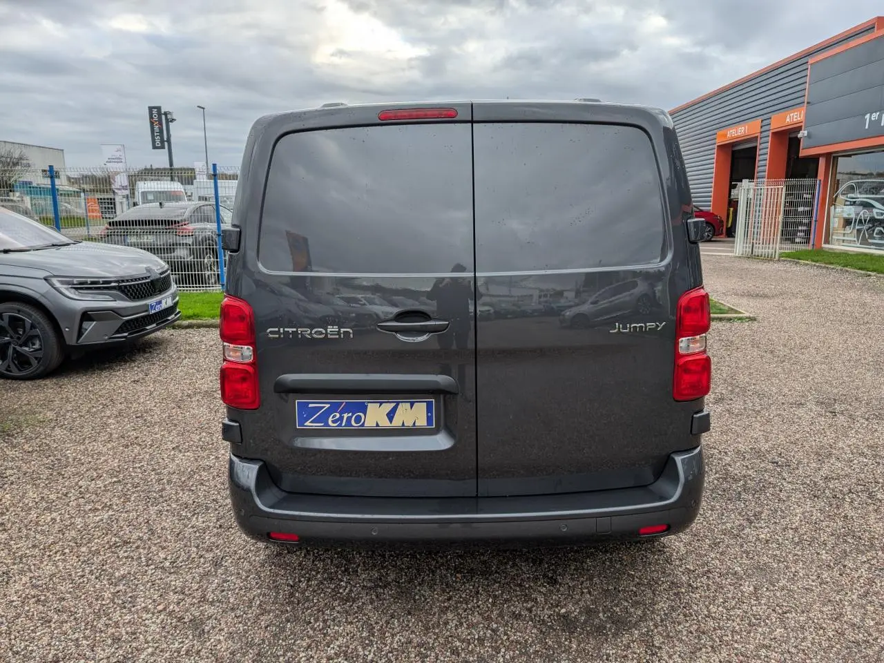 Vue arrière d'un Citroën Jumpy gris foncé avec portes battantes et feux rouges visibles sur un parking.