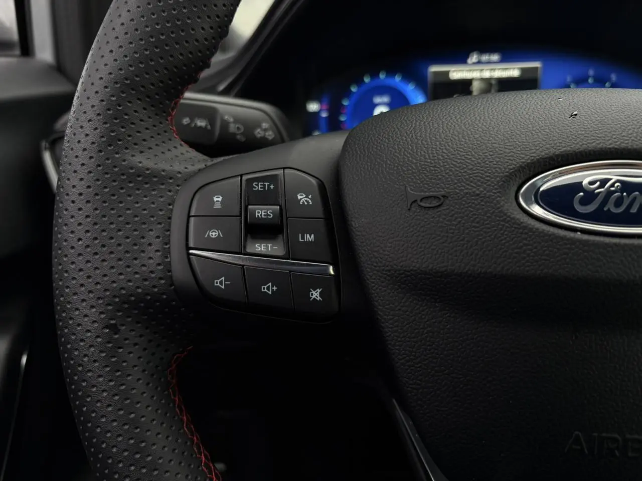 Gros plan sur le volant perforé noir avec surpiqûres rouges du Ford Puma 2023, montrant les commandes multifonctions à gauche.