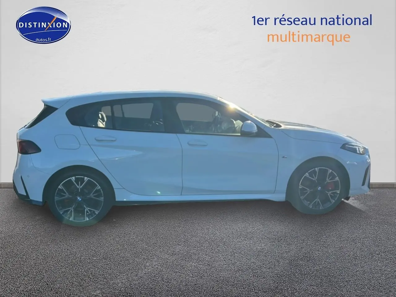 Profil droit d'une BMW Série 1 blanche alpin avec jantes 18 pouces bicolores en Y, sur fond clair intérieur showroom.