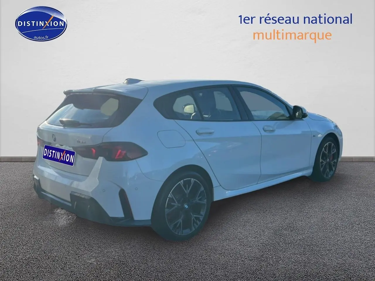 BMW Série 1 blanche vue en 3/4 arrière droit, avec jantes 18 pouces bicolores et becquet arrière sportif.