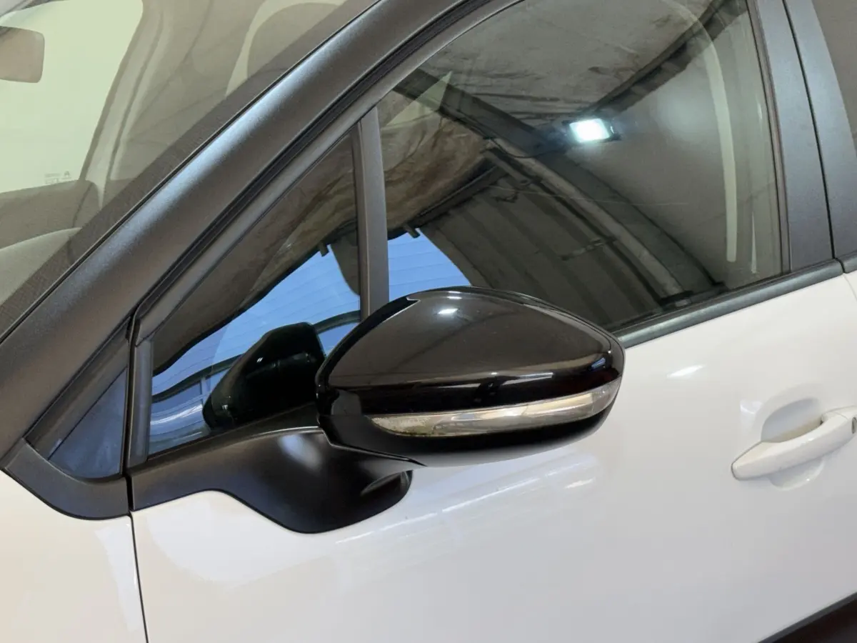 Gros plan sur le rétroviseur noir brillant côté conducteur d'une Citroën C3 blanche, avec la porte avant visible.