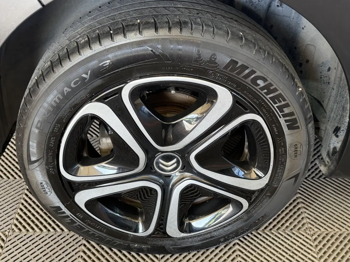 Gros plan sur la roue avant droite d'une Citroën C3 blanche, mettant en valeur la jante noire et argentée avec logo Citroën central.