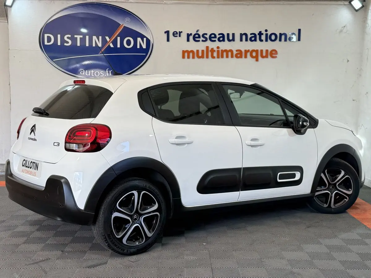Citroën C3 blanc vue de côté droit en intérieur, avec protections latérales noires et jantes alliage distinctives.