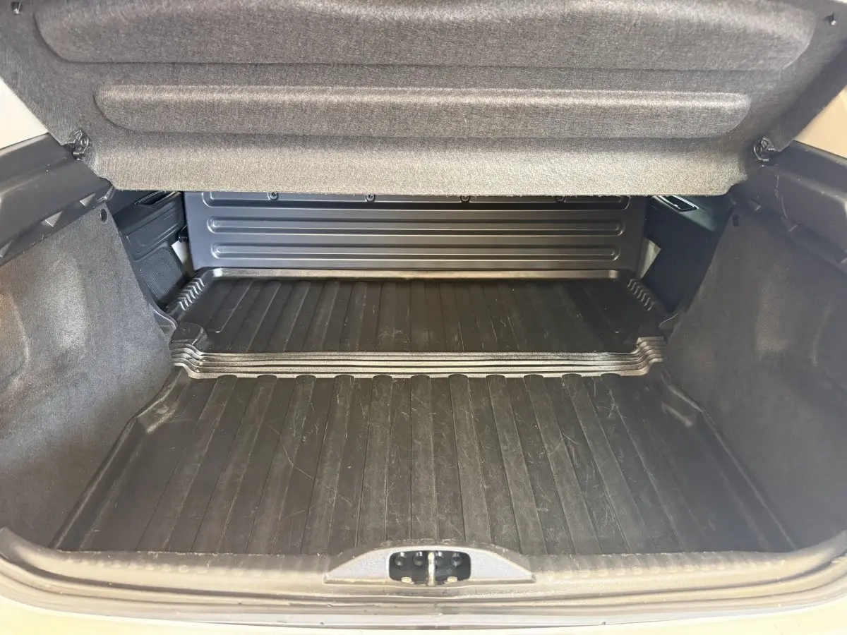 Vue intérieure du coffre ouvert de la Citroën C3 blanche, montrant le tapis de protection noir et les parois rembourrées.