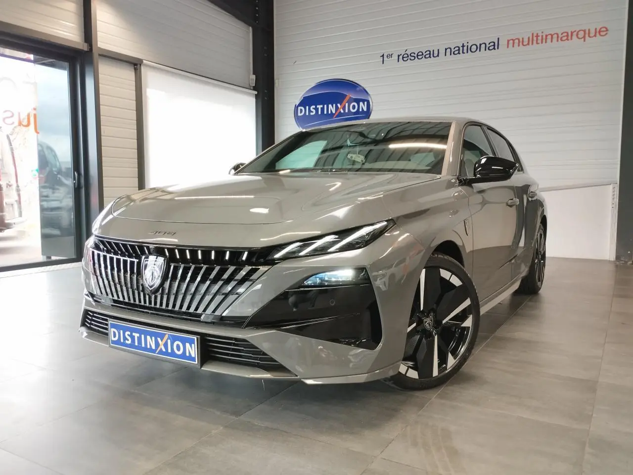 Peugeot 308 hybride gris selenium vue 3/4 avant droit, calandre verticale chromée et jantes alliage noires.