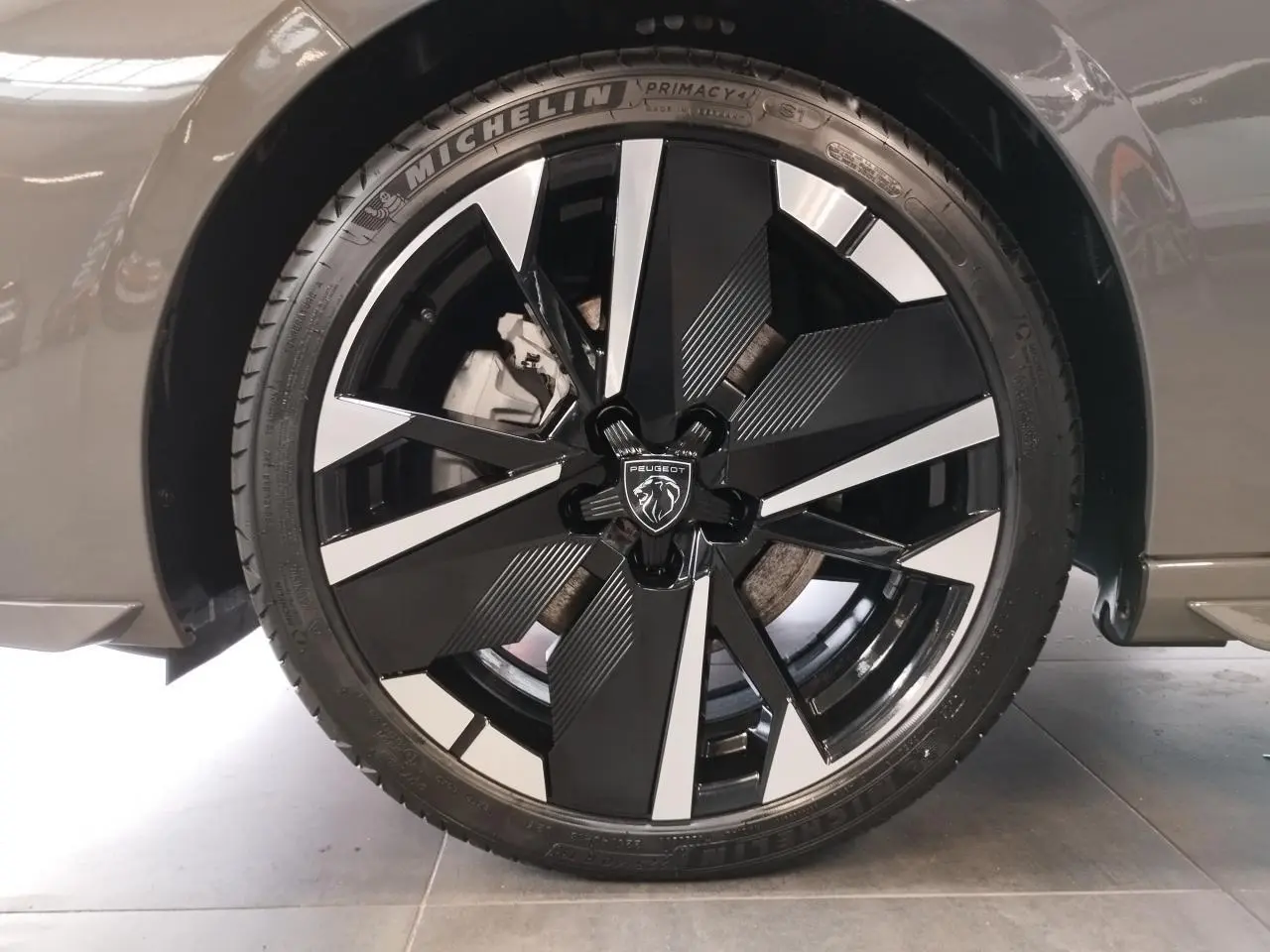 Gros plan sur la jante alliage 18" bi-ton noir et argent avec logo Peugeot, sur roue avant droite gris sélénium.