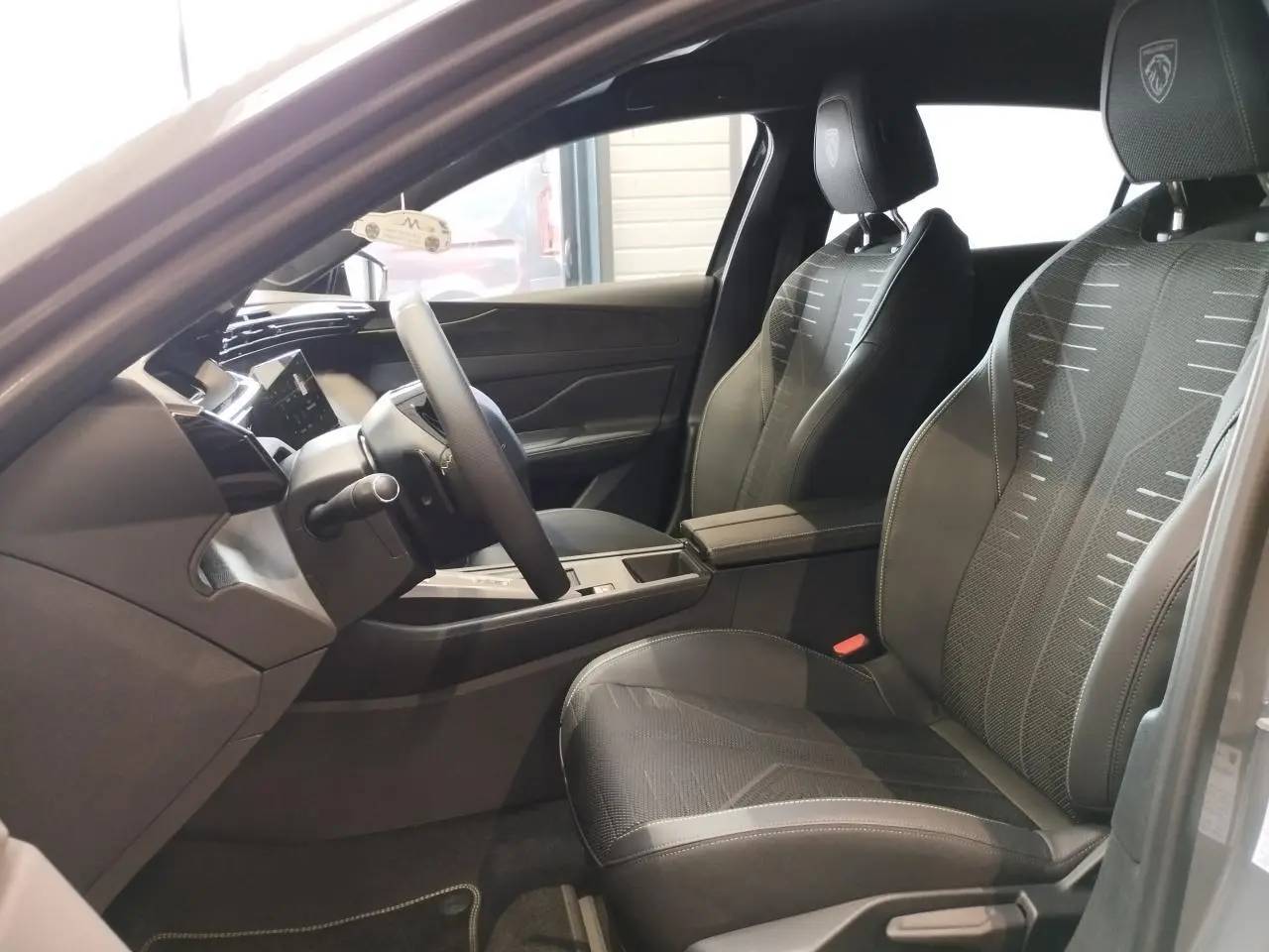 Intérieur avant droit de la Peugeot 308 gris selenium, sièges noirs avec surpiqûres vert Adamite et logo Peugeot brodé.