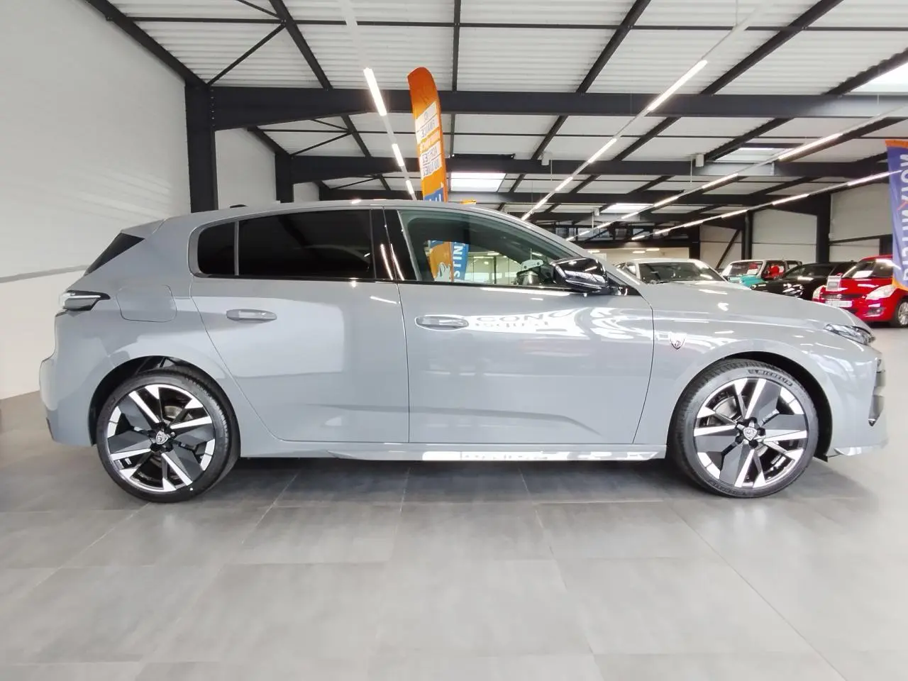 Vue de profil droit d'une Peugeot 308 gris selenium avec jantes alliage bi-tons et vitres surteintées dans un showroom.
