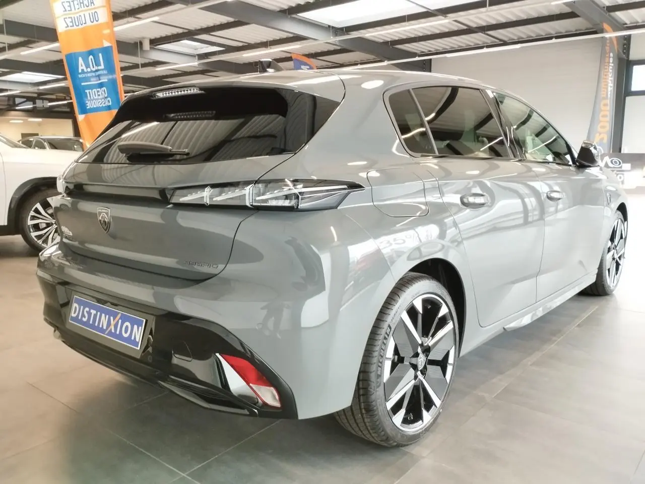 Vue 3/4 arrière droite d'une Peugeot 308 hybride gris selenium avec jantes alliage bi-tons et feux arrière à LED 3 griffes.