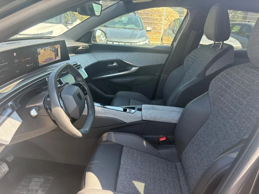 Vue intérieure côté conducteur du Peugeot 3008 Hybrid 145 e-DCS6 Allure 2025, sièges tissu gris et cuir noir, tableau de bord numérique.