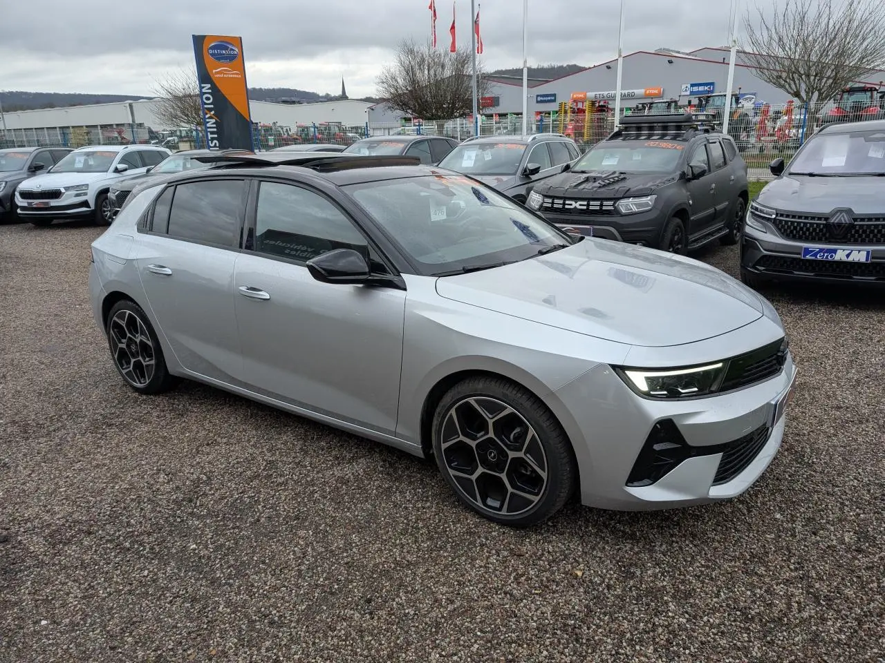 Opel Astra 2024 gris métallisé vue 3/4 avant avec toit noir panoramique et jantes alliage 18 pouces pentagonales.
