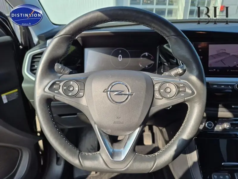 Vue centrée sur le volant cuir multifonction de l'Opel Grandland noir, avec tableau de bord digital en arrière-plan.