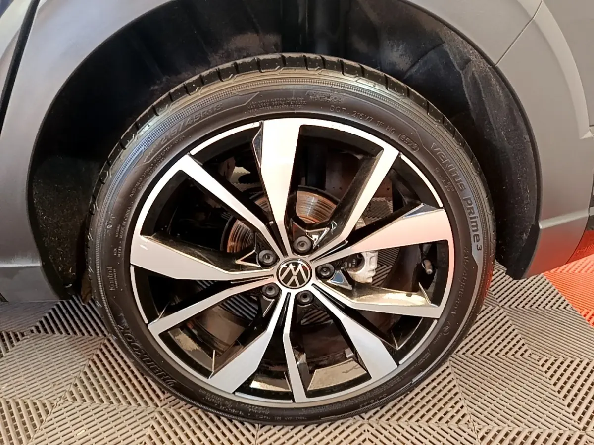 Gros plan sur la roue avant droite du Volkswagen Taigo noir, avec jante alliage bicolore et logo VW au centre.