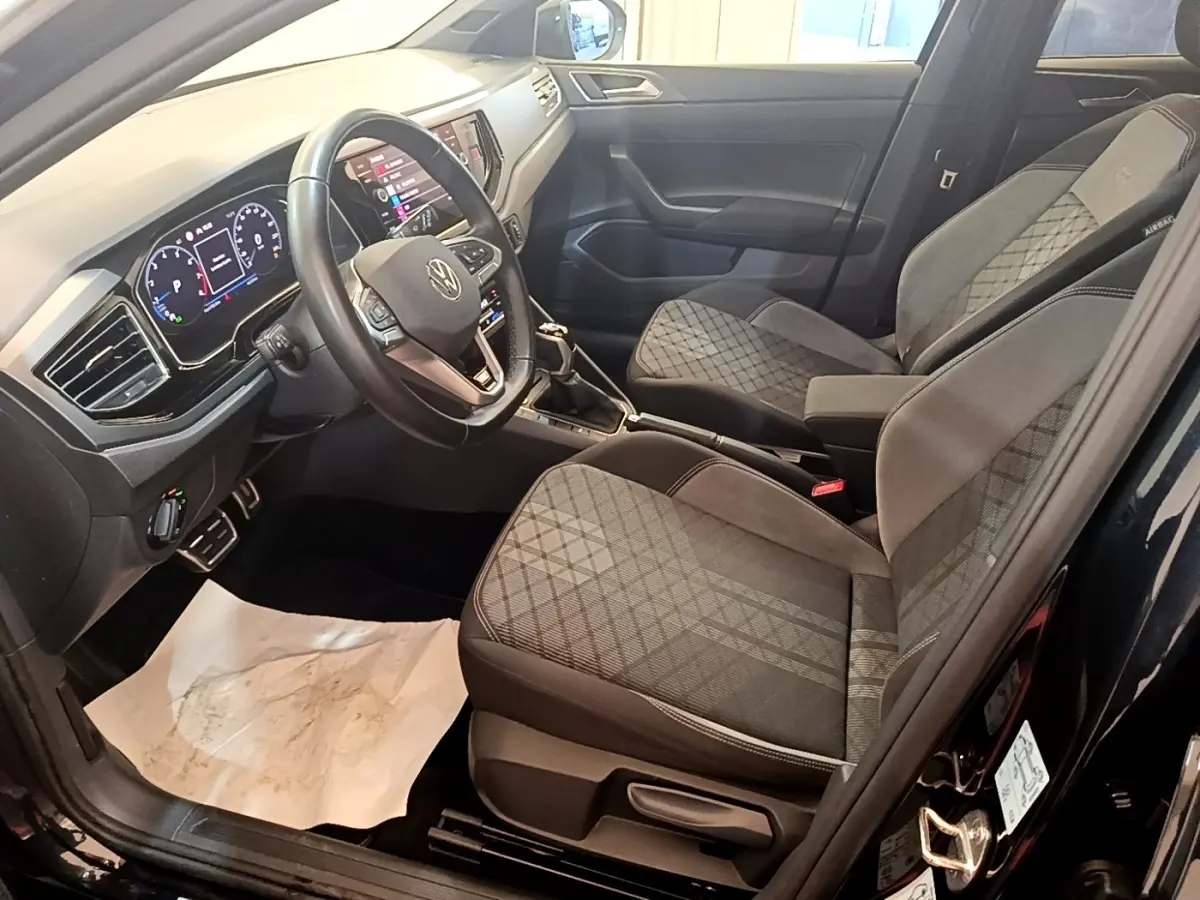 Vue intérieure côté conducteur du Volkswagen Taigo noir 2023, sièges tissu à motifs et tableau de bord digital.