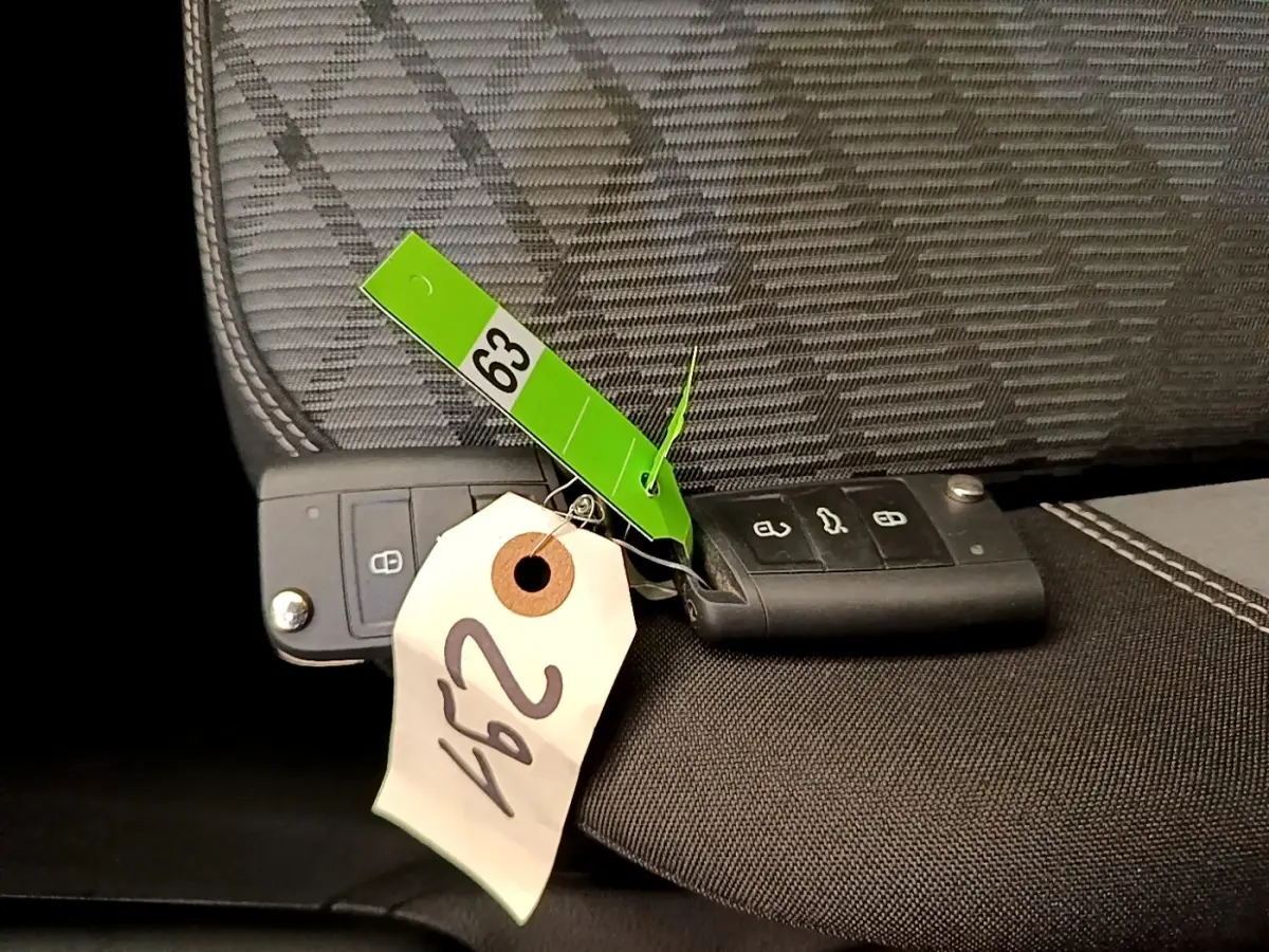 Gros plan sur deux clés noires Volkswagen posées sur un siège tissu gris et noir avec étiquettes numérotées.