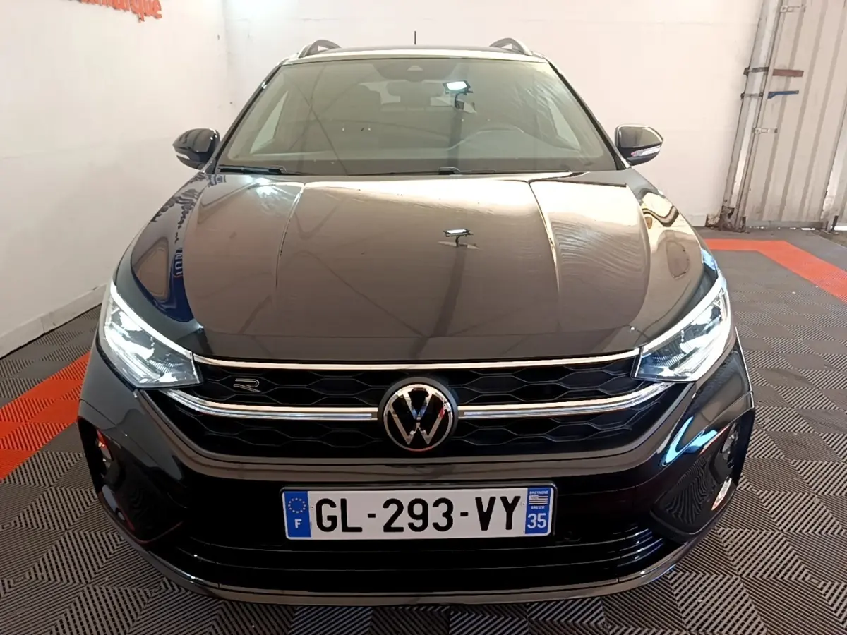 Vue frontale d’un Volkswagen Taigo 1.5 TSI R-Line noir avec phares LED et calandre chromée en intérieur showroom.