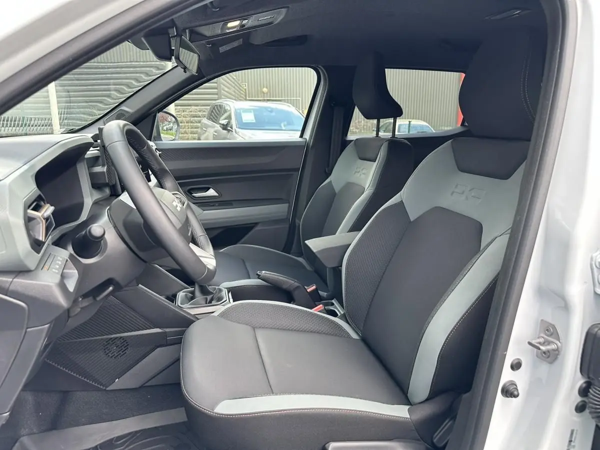 Vue intérieure côté conducteur du Dacia Duster blanc glacier 2025, montrant les sièges avant bi-ton et le volant.
