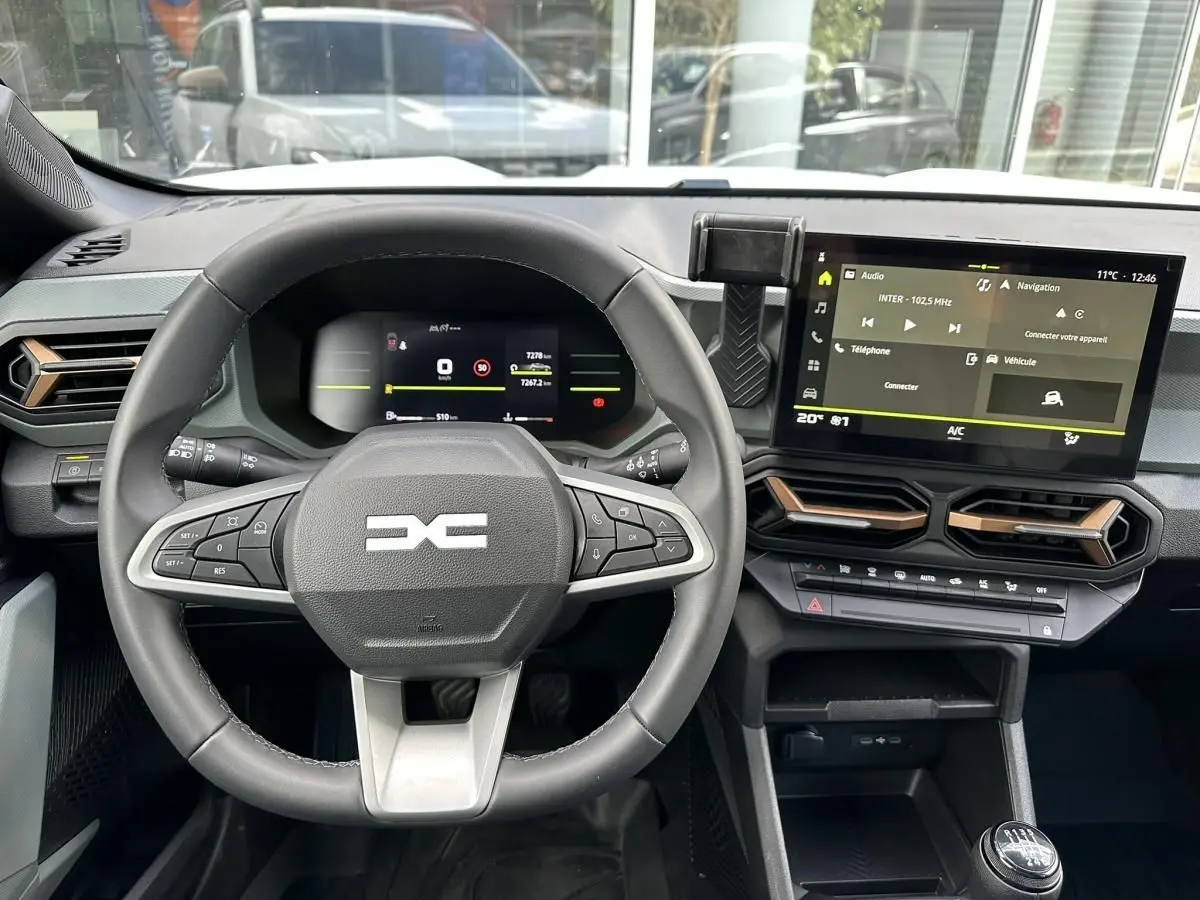 Vue intérieure centrée sur le volant et le tableau de bord numérique du Dacia Duster blanc glacier 2025.