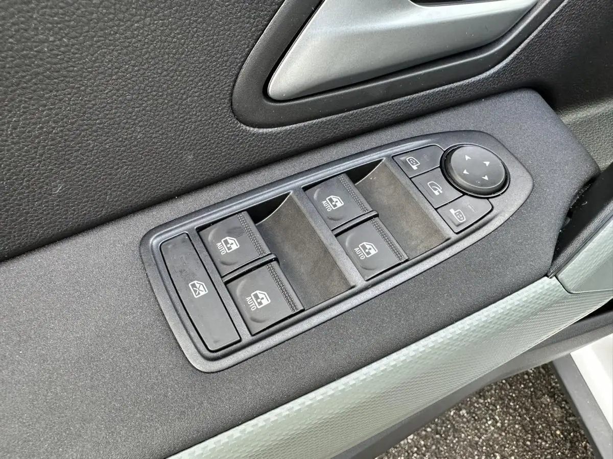 Gros plan sur les commandes des vitres et rétroviseurs côté conducteur du Dacia Duster blanc glacier 2025.