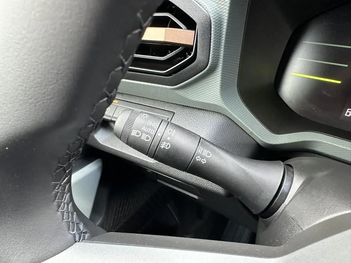 Gros plan sur la commande des feux et clignotants à gauche du volant dans l’habitacle du Dacia Duster blanc glacier 2025.