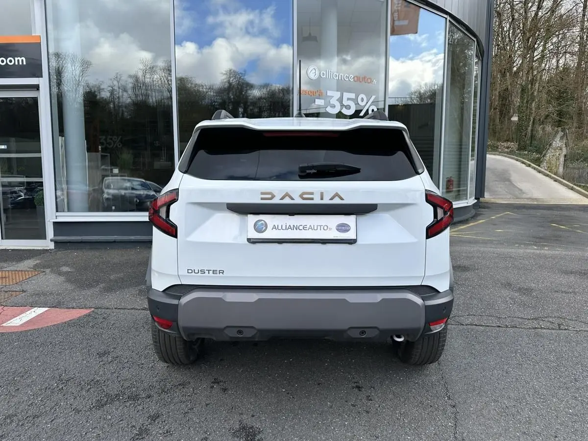 Vue arrière du Dacia Duster blanc glacier 2025 avec vitres surteintées et logo DACIA en relief doré.