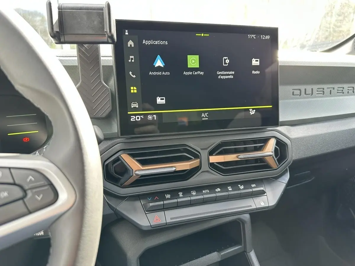 Vue intérieure du tableau de bord du Dacia Duster 2025, avec écran tactile central et aérateurs hexagonaux bronze.