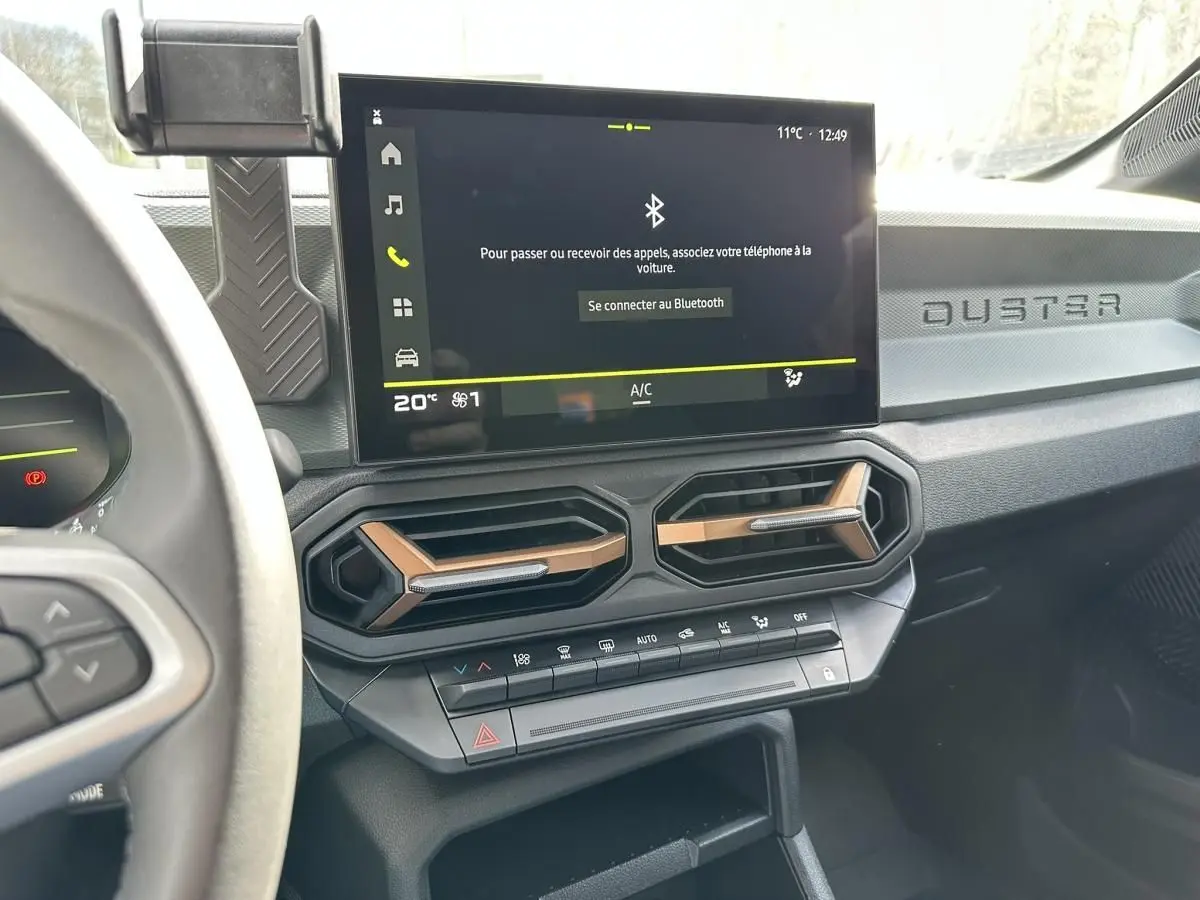 Tableau de bord du Dacia Duster 2025 avec écran tactile, aérateurs hexagonaux et inscription DUSTER côté passager.