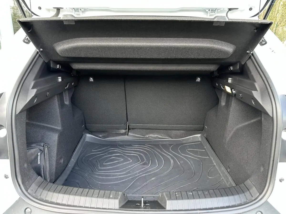 Coffre ouvert vu de l'arrière d'un Dacia Duster blanc glacier, avec tapis de sol noir et intérieur sombre.
