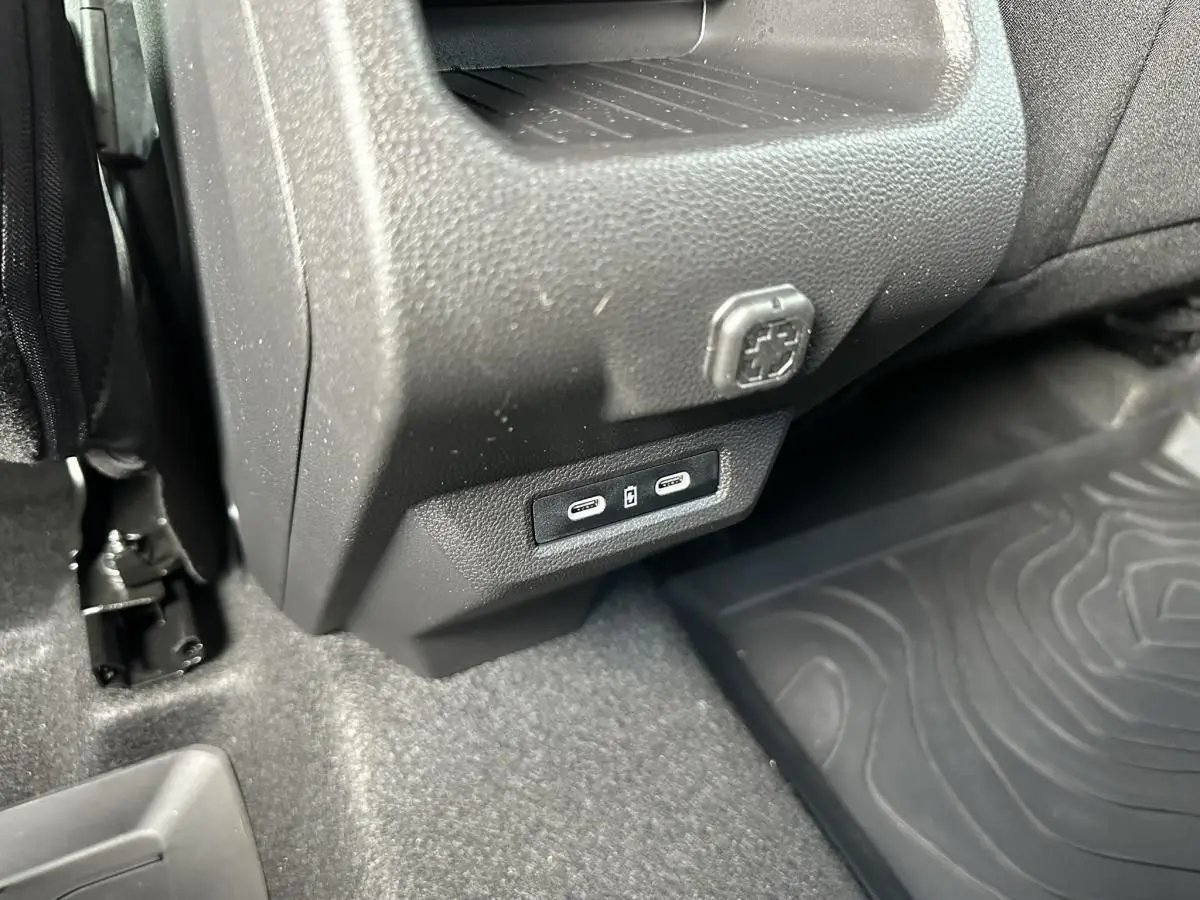 Détail intérieur montrant les ports USB-C et une prise 12V sous la console centrale du Dacia Duster blanc glacier.