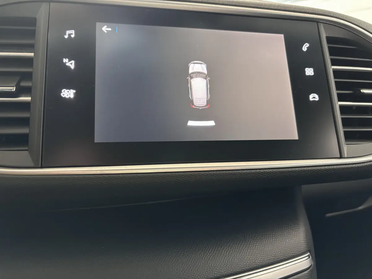 Écran tactile central de la Peugeot 308 gris foncé affichant l'aide au stationnement en vue aérienne.