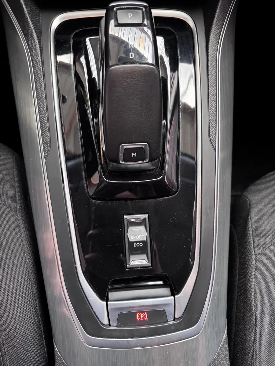Vue rapprochée de la console centrale noire et grise avec levier de vitesses automatique et bouton modes Sport/Eco d'une Peugeot 308 gris foncé.