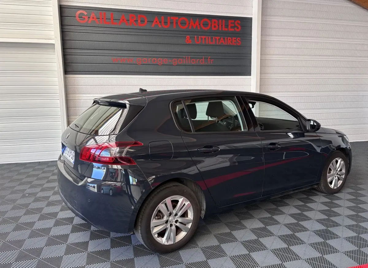 Vue 3/4 arrière droite d'une Peugeot 308 gris foncé garée en intérieur sur sol à damier.