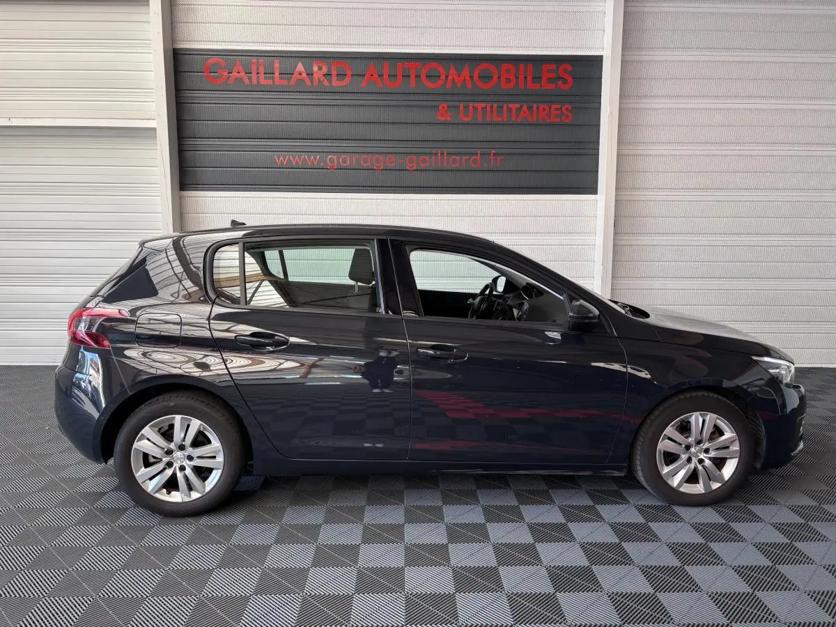 Profil côté gauche d'une Peugeot 308 gris foncé de 2019 garée en intérieur sur sol damier.