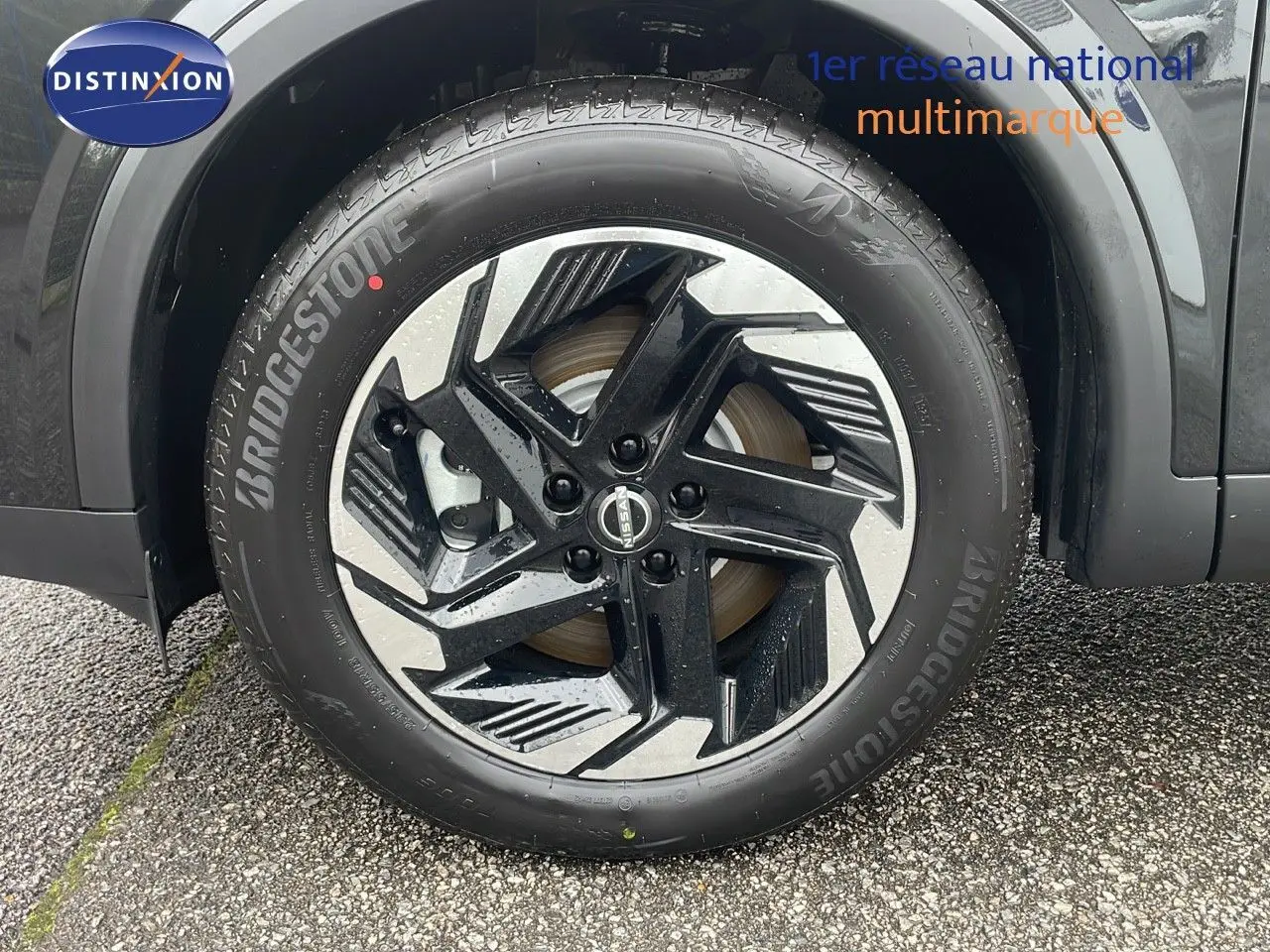 Gros plan sur la roue avant gauche du Nissan Qashqai noir perle métal avec jante alliage bicolore distinctive.