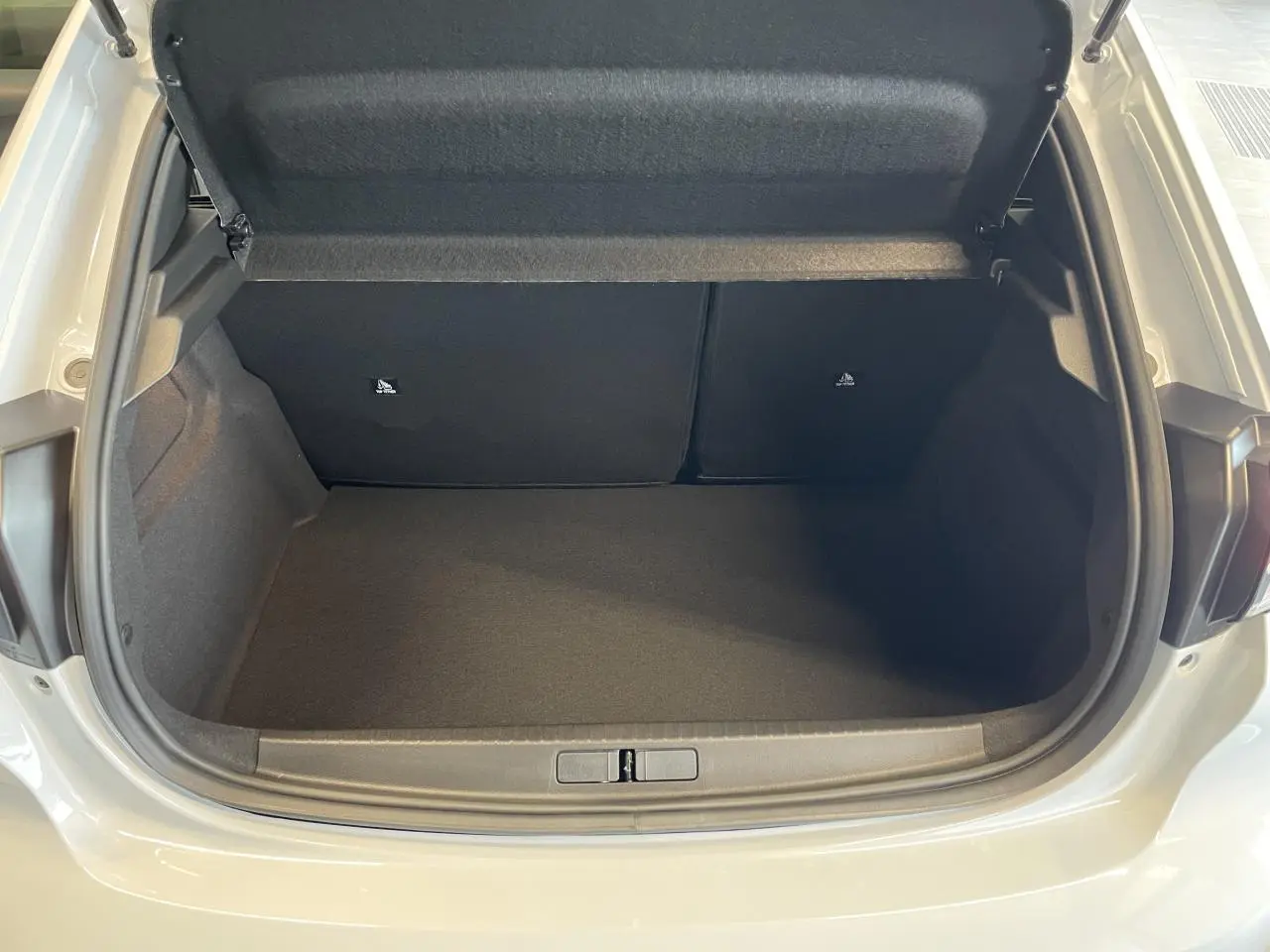 Coffre ouvert vu de l'arrière d'une Peugeot 208 blanche Okenite, montrant l'espace de rangement vide et la doublure noire.