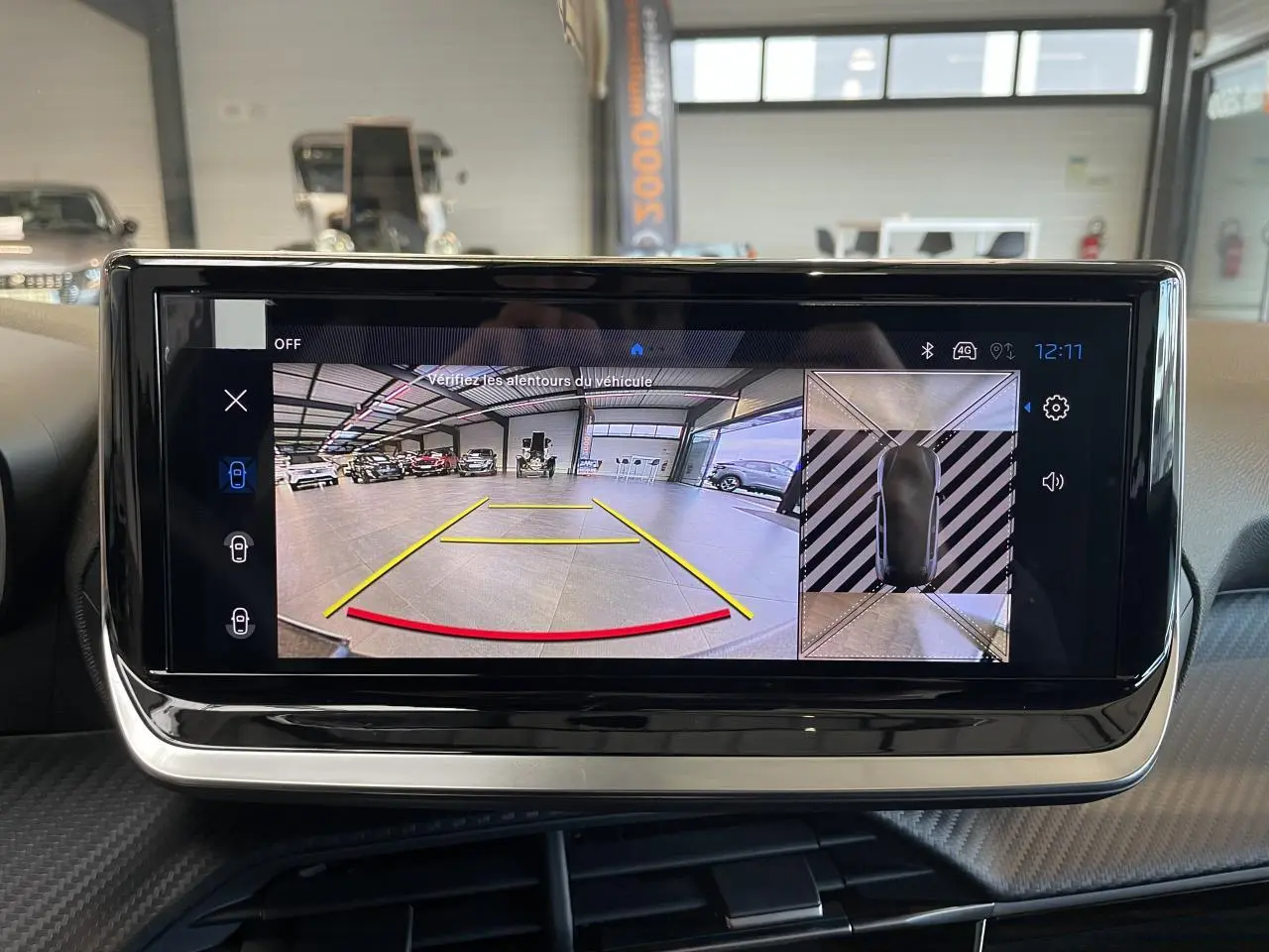 Écran tactile intérieur montrant la caméra de recul et la vue 360° du Peugeot 208 hybride blanc Okenite.