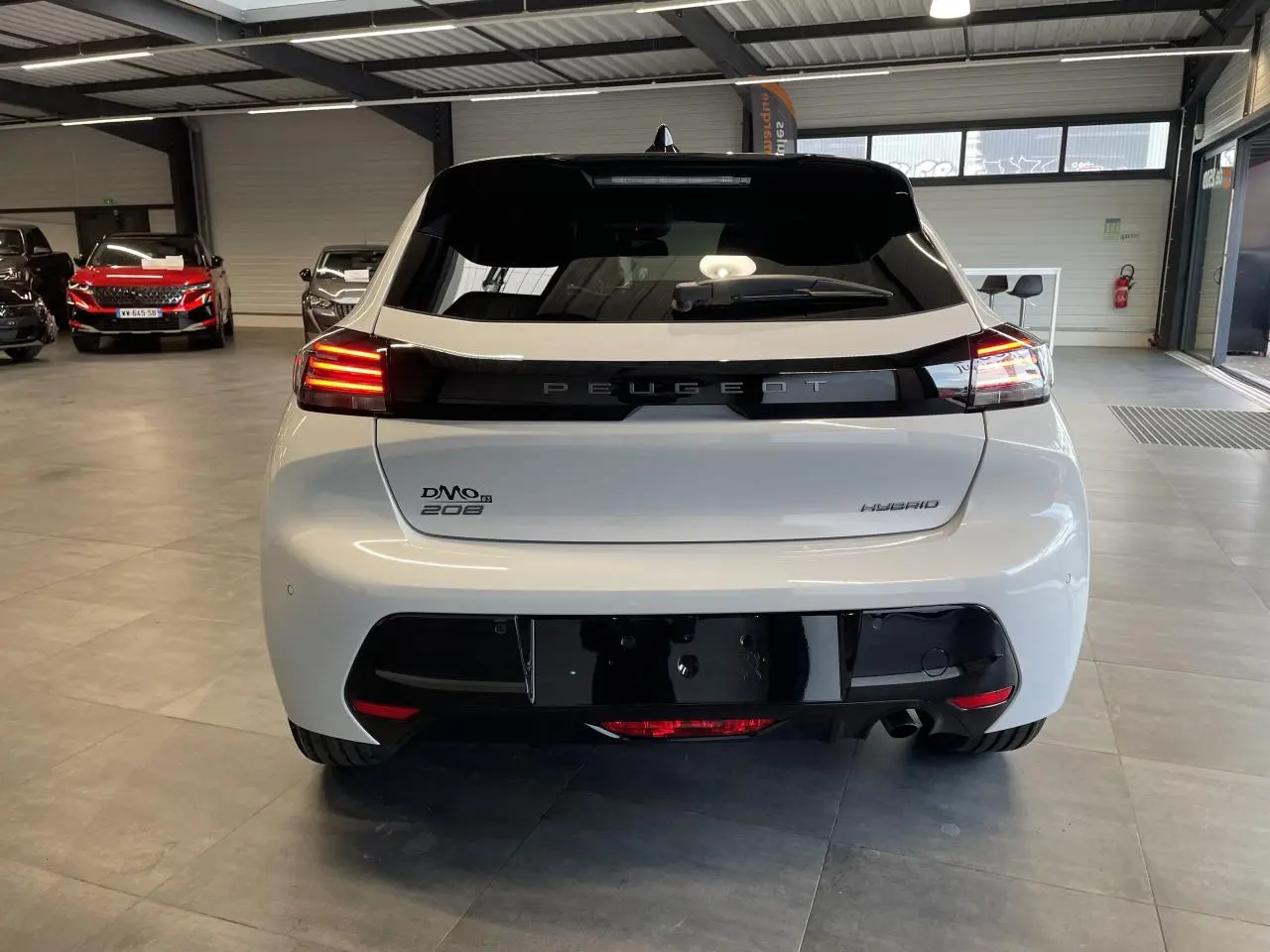 Vue arrière d'une Peugeot 208 hybride blanche Okenite avec bandeau noir brillant et feux arrière LED 3 griffes allumés.