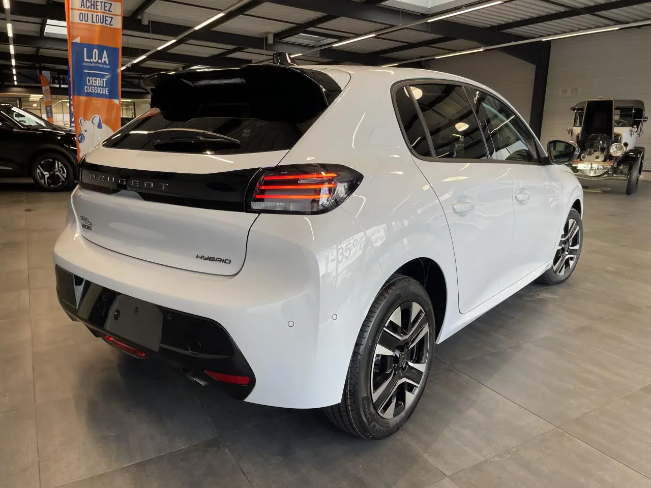 Vue 3/4 arrière droite d'une Peugeot 208 hybride blanche Okenite avec bandeau noir brillant entre les feux LED.