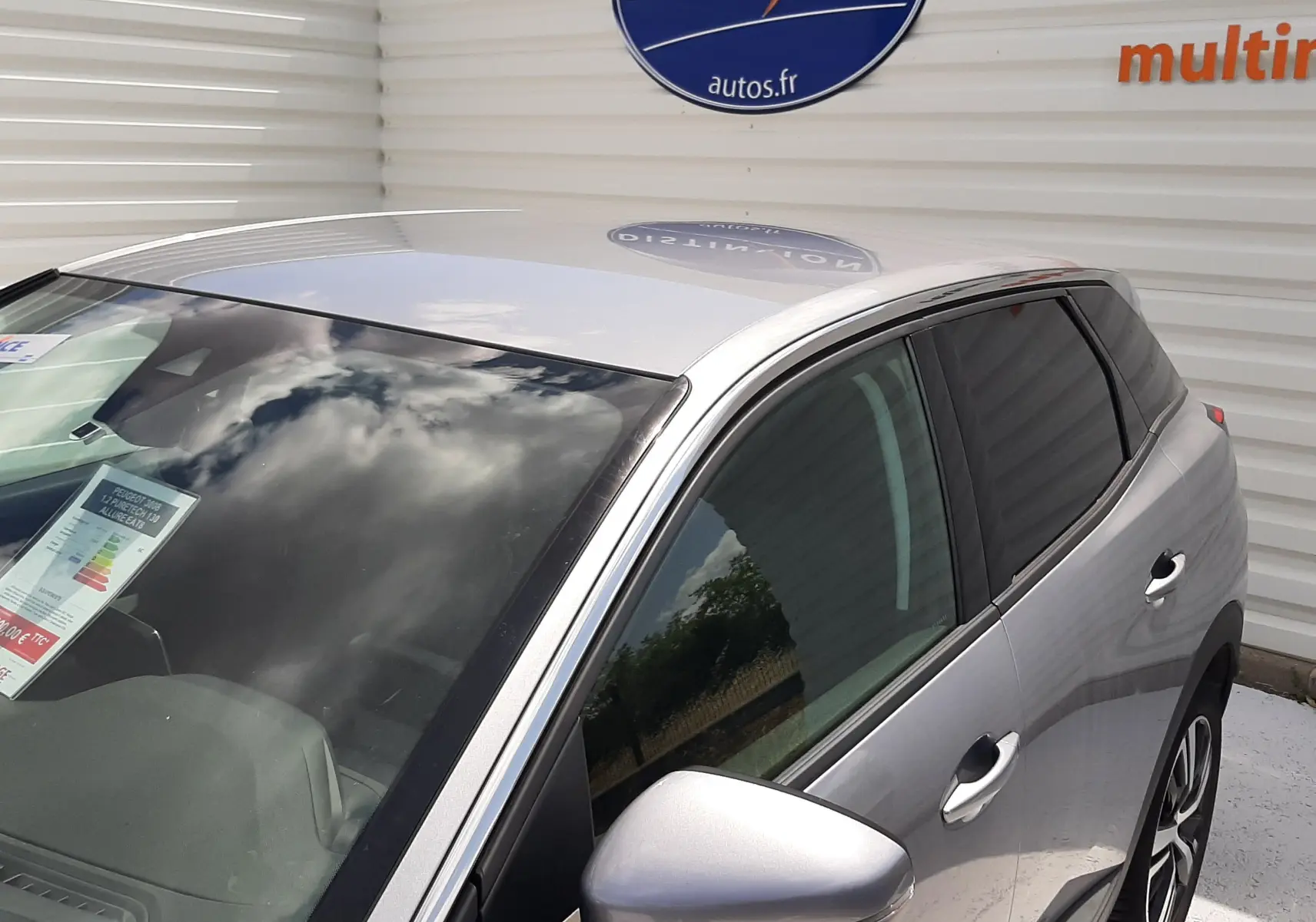 Vue 3/4 avant droit d'un Peugeot 3008 gris métallisé garé devant un mur blanc avec logo Distinxion visible.